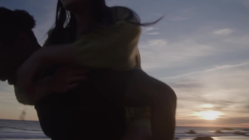 Woman climbing onto a mans back on the beach in the late afternoon