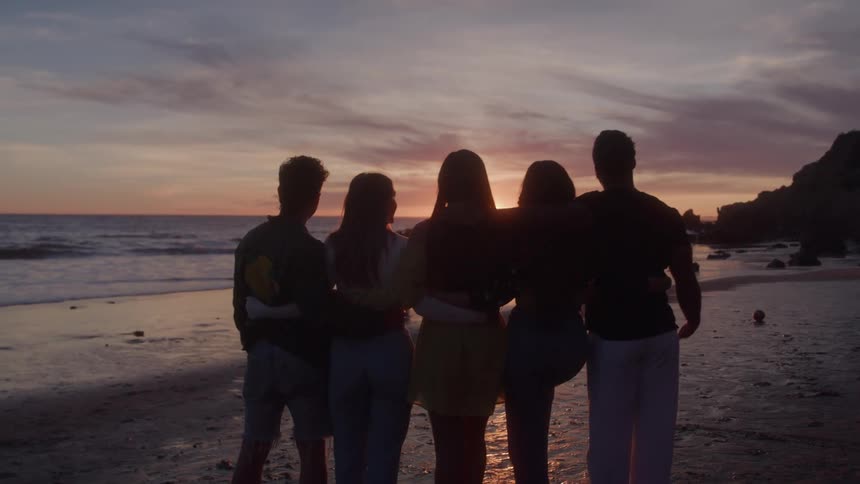 In the first clip a group of five friends stands silhouetted against a beautiful sunset on a beach the second clip shows a figure in a white spacesuit walking through a dark hallway which is lit by an eerie red light
