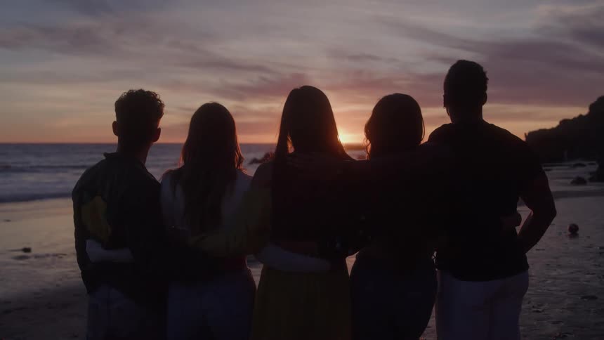Groups of friends hugging on the beach watching the sunset