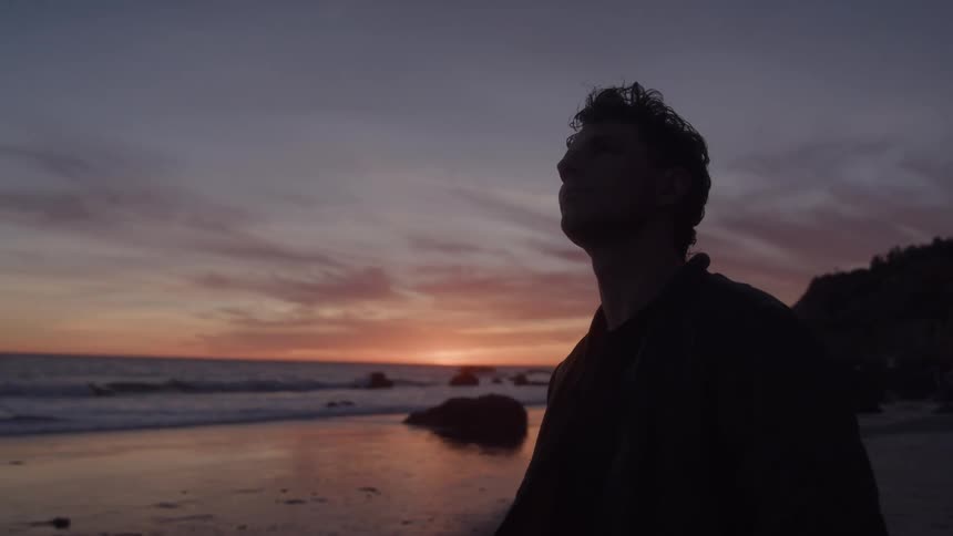 Close up portrait of a young man standing outdoors at the beach at sunset