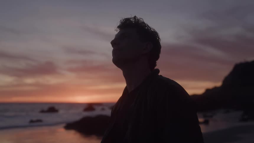 Man watching the sunset by the sea in silhouette against the colorful sky