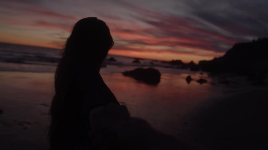 Silhouette of a woman holding hands walking on the beach at dusk