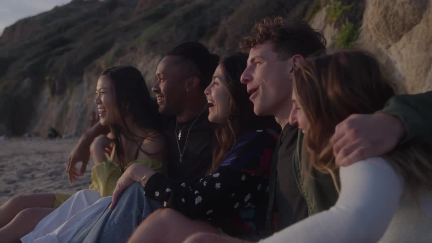 A group of people sits on a beach laughing and looking forward