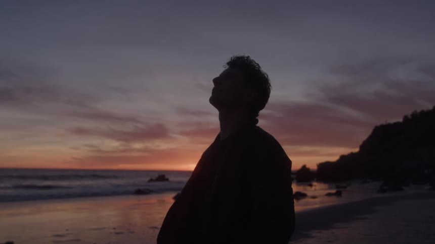 The man looks up on the beach as the sun sets