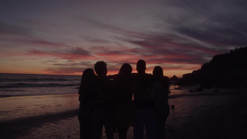 Friends hug on the beach and watch the sun set