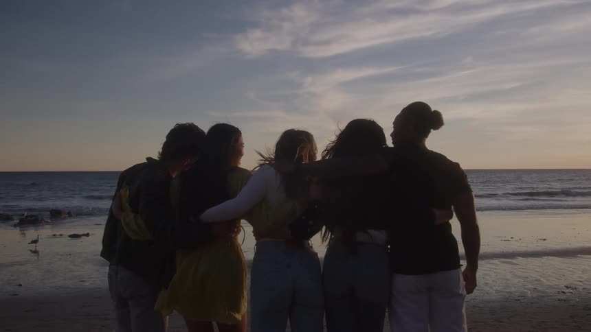 Group of five friends hugging in front of the sea at dawn