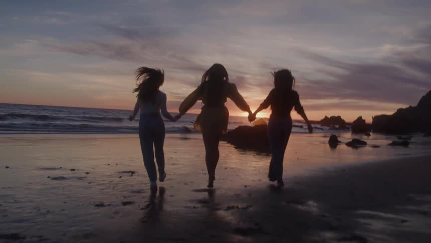 Women hold hands and skip on the beach