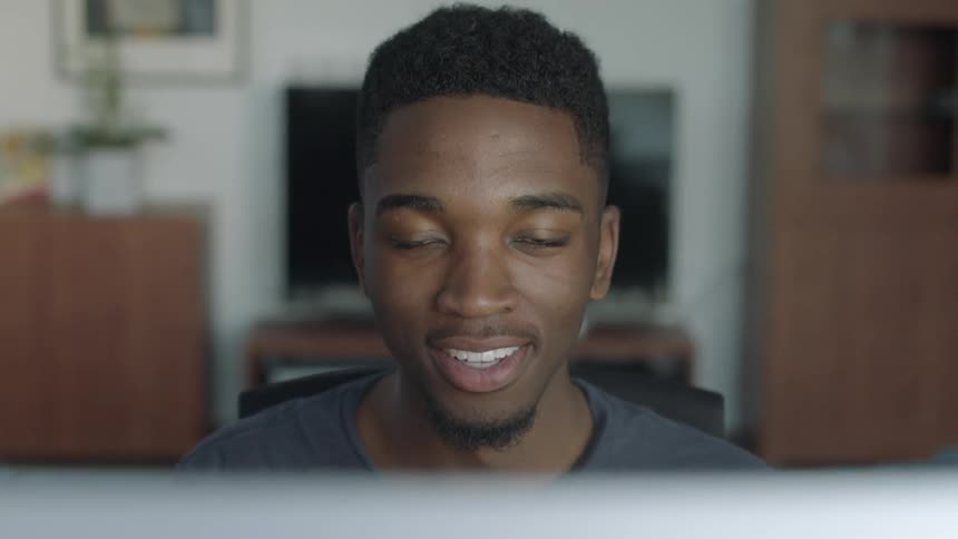 A man sits at a computer while smiling and nodding his head