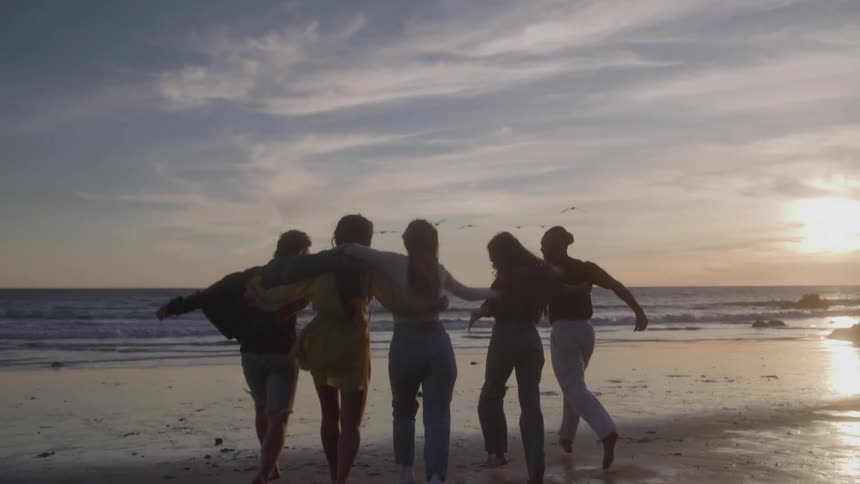 A group of people runs and jumps along a beach with the ocean behind them