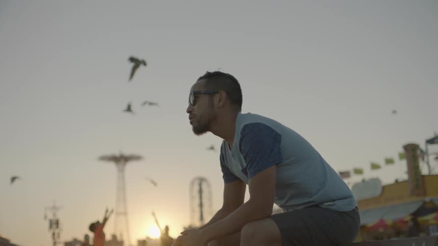 A man is sitting on the boardwalk at sunset