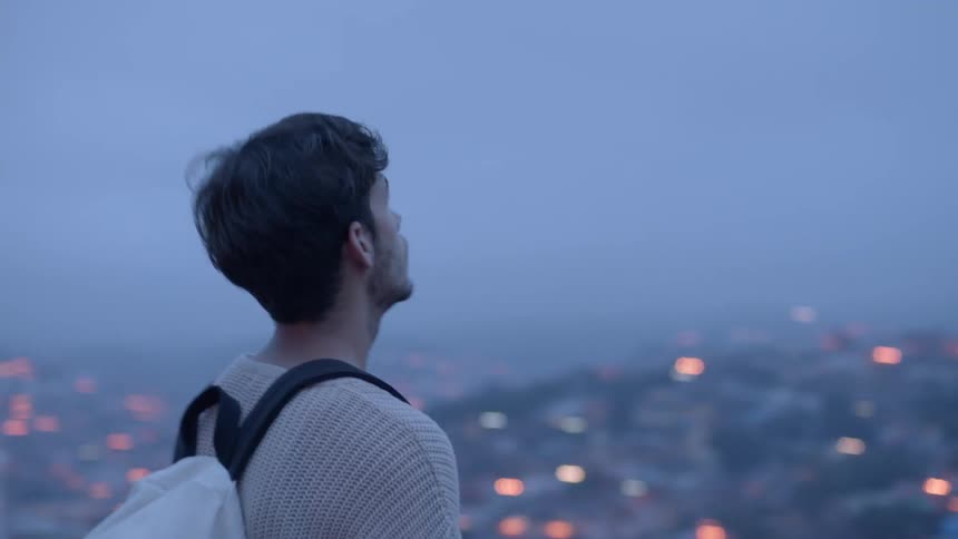 A man stands above a city looking out at the view