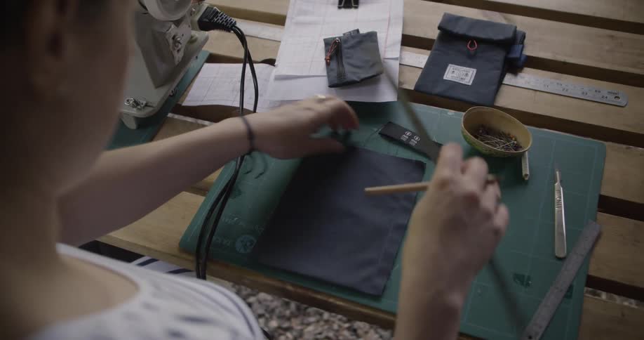 A woman wearing a ring smooths fabric on a cutting mat while preparing sewing materials with rulers and pins