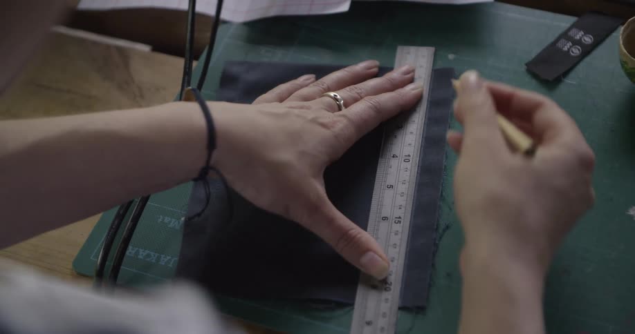 A person marks fabric with a ruler and pencil in a studio