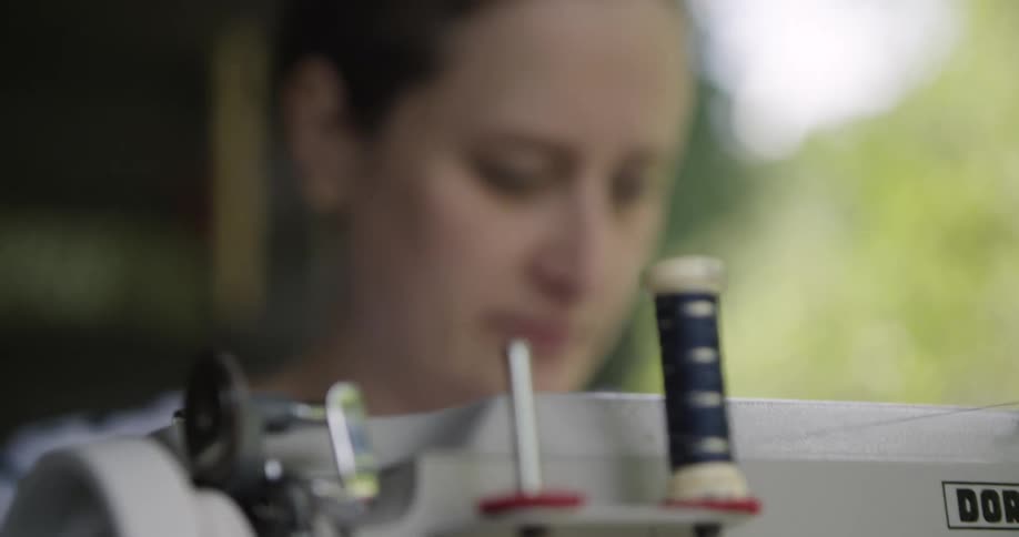A woman focuses on sewing with a machine outdoors