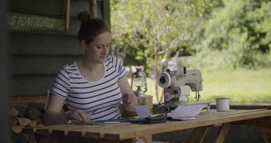A woman measures fabric beside a sewing machine outdoors
