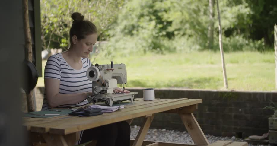 The woman uses a sewing machine outside her home