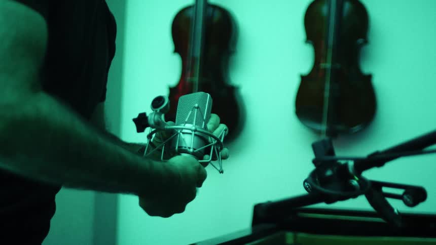 Man standing in a music studio attaches a microphone onto an arm stand