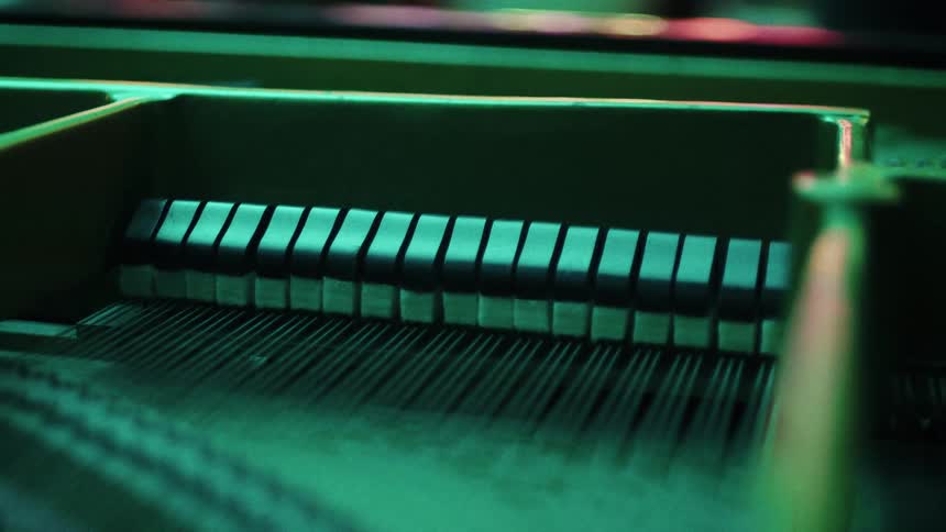 The inner mechanics of a piano with hammers and strings under green lighting