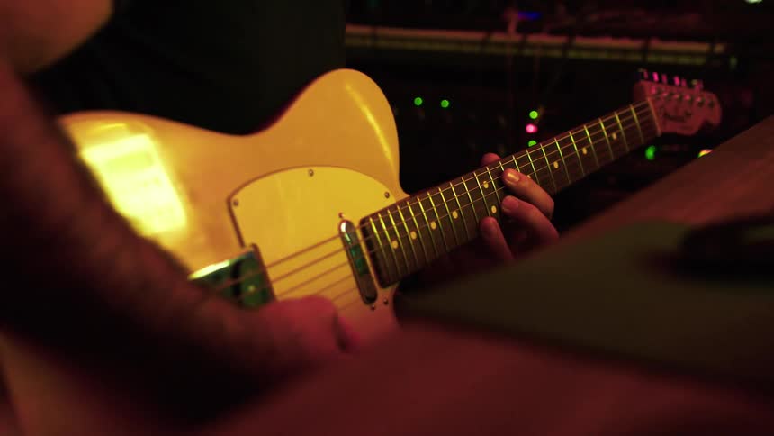 A musician plays an electric guitar in a dimly lit studio