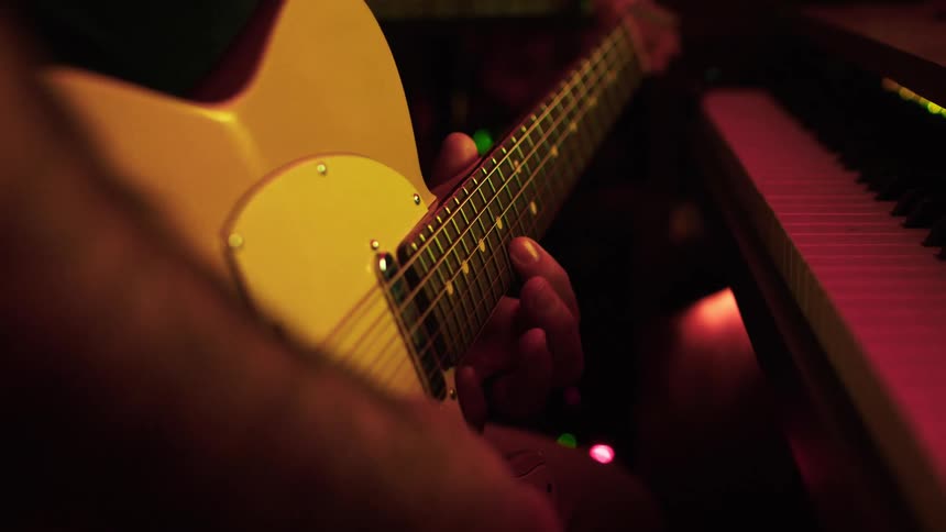 A mans hands playing an electric guitar on a studio setting with a piano in front