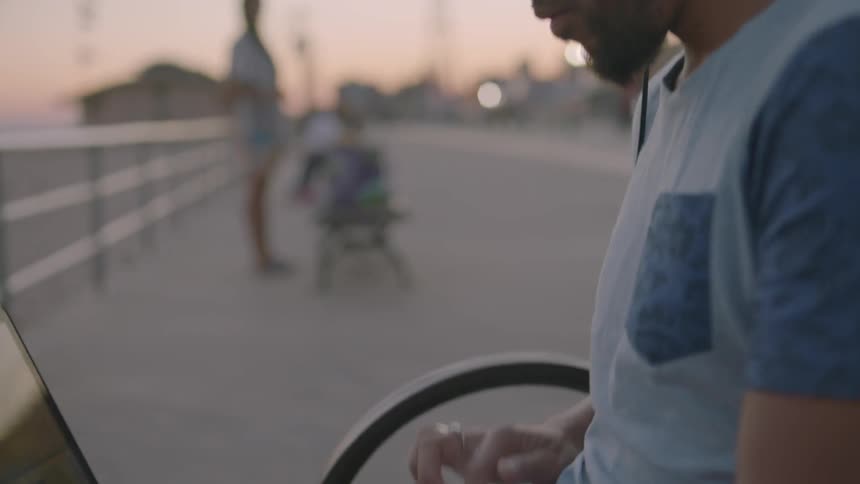 A man works on a computer on an outdoor bench at sunset