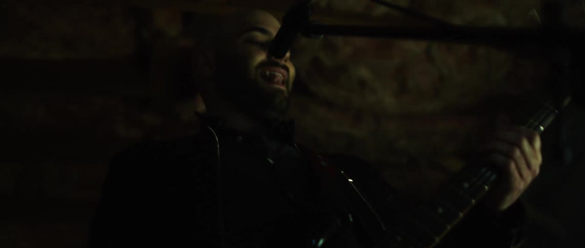 Guitarist sings during a band performance under a ceiling with exposed rafters