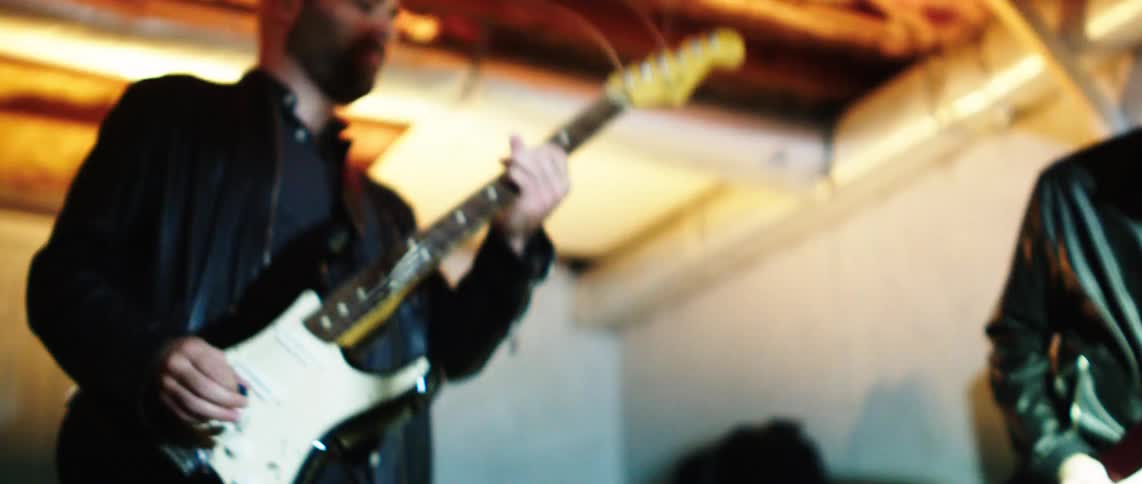 A couple of musicians in black leather jackets are playing electric guitars on a stage under flashing lights