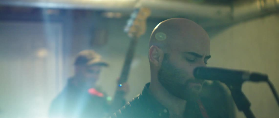 Man singing in a performance with another member of the group playing guitar in the background