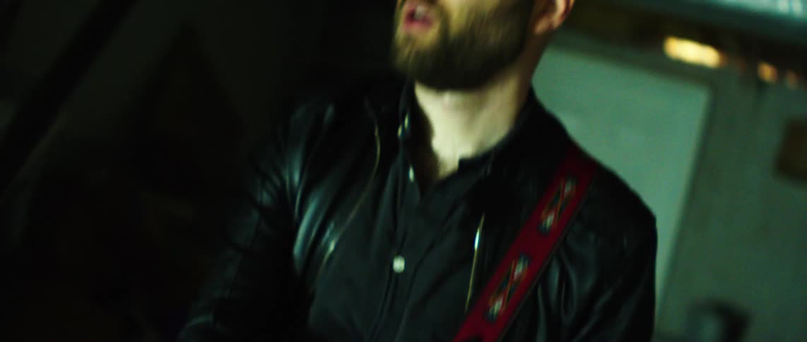 Guitarist plays his guitar while in a messy room lit by red lighting