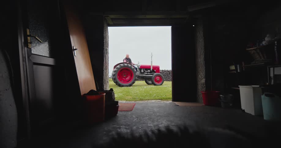 Man backing up a tractor seen through a shed on the farm