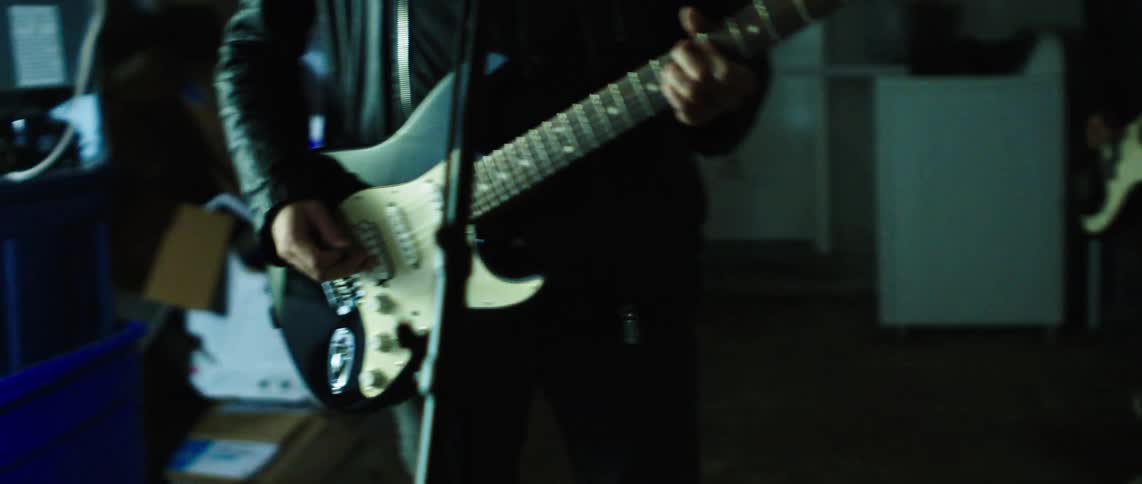 Guitarists play in a messy room under flashing lights