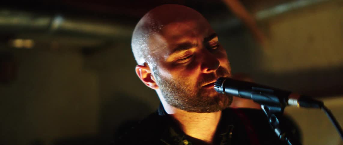 Guitarist sings during a band performance in a room lit by colored lighting