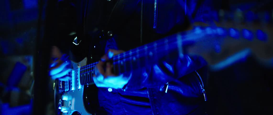 Guitarists play rapidly while backlit by a spotlight