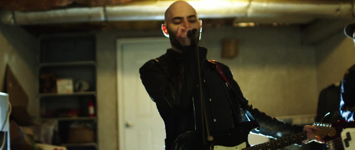 The band member sings into the mic as they both play guitar