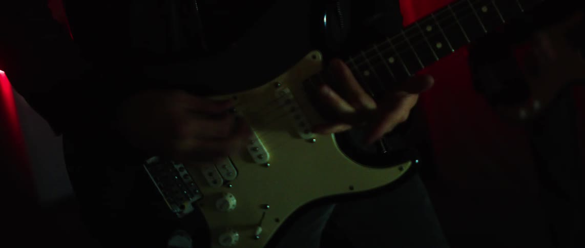 Musician playing a black electric guitar with a white pickguard