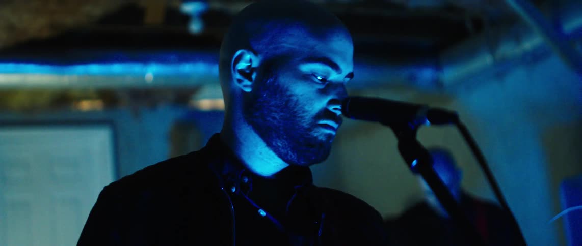 A musician in a band performs into a microphone under different stage lighting