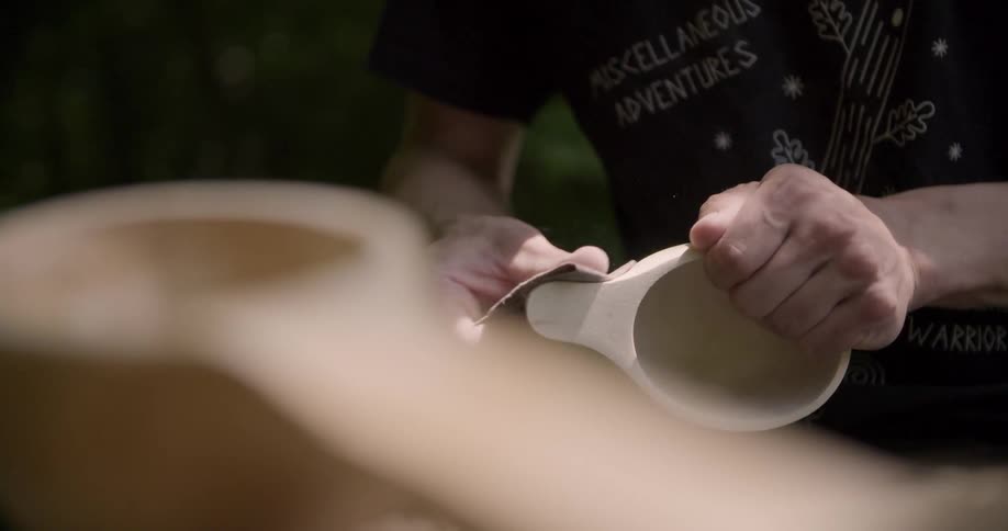 A persons hands holds a piece of wood and sands it with a piece of sandpaper
