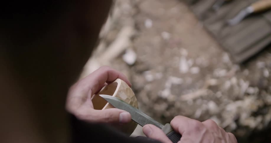 The man is carving a bowl with a small blade