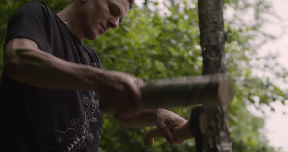 A person chops a log with an axe in a dense forest at midday