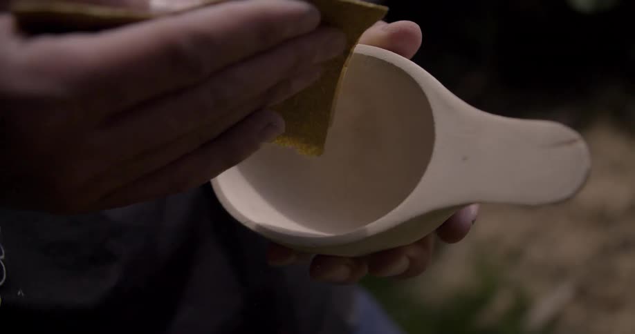 The man is sanding a small wooden cup