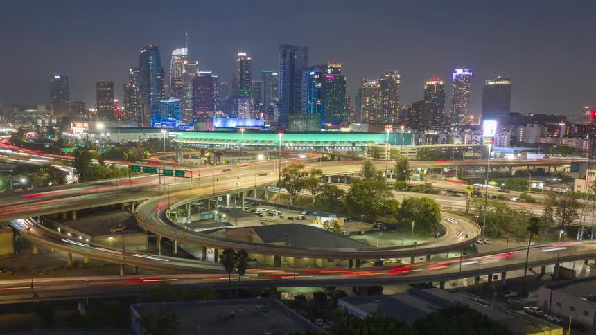 Busy highway at night with streams of cars moving in both directions cityscape and convention center of Los Angeles in the background the scene illuminated by bright lights
