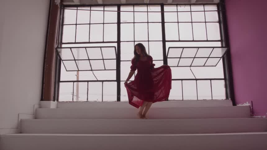 A woman in a red dress poses gracefully on stairs by large windows