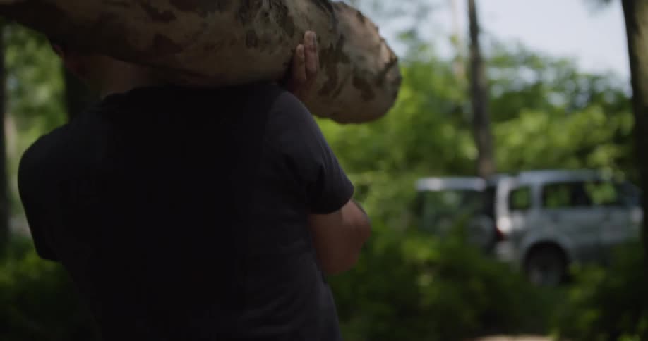 A man carries a large tree log on his shoulder in the forest