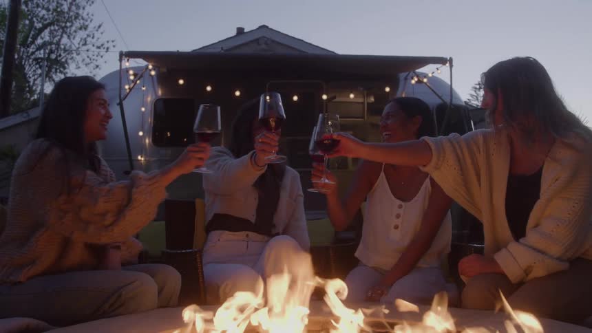 Four women toast with wine glasses around the fire pit