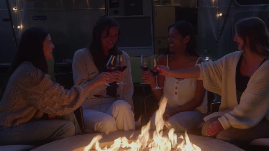 Women make a toast together in front of the fire pit