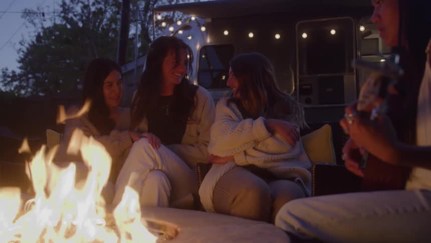 Group of four women sitting around a campfire with one of them playing the guitar