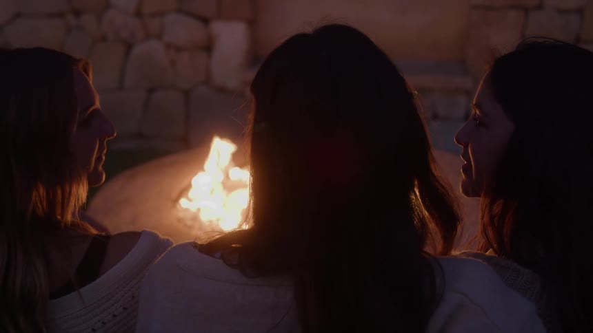 Three people sitting around a lit bonfire