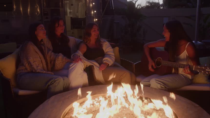Four women around a fire pit with one playing the guitar