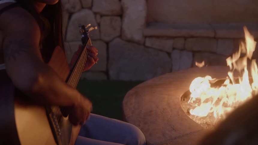 Woman sitting next to a campfire playing guitar