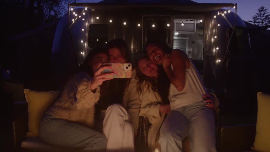 Women are sitting by the fire taking a selfie together
